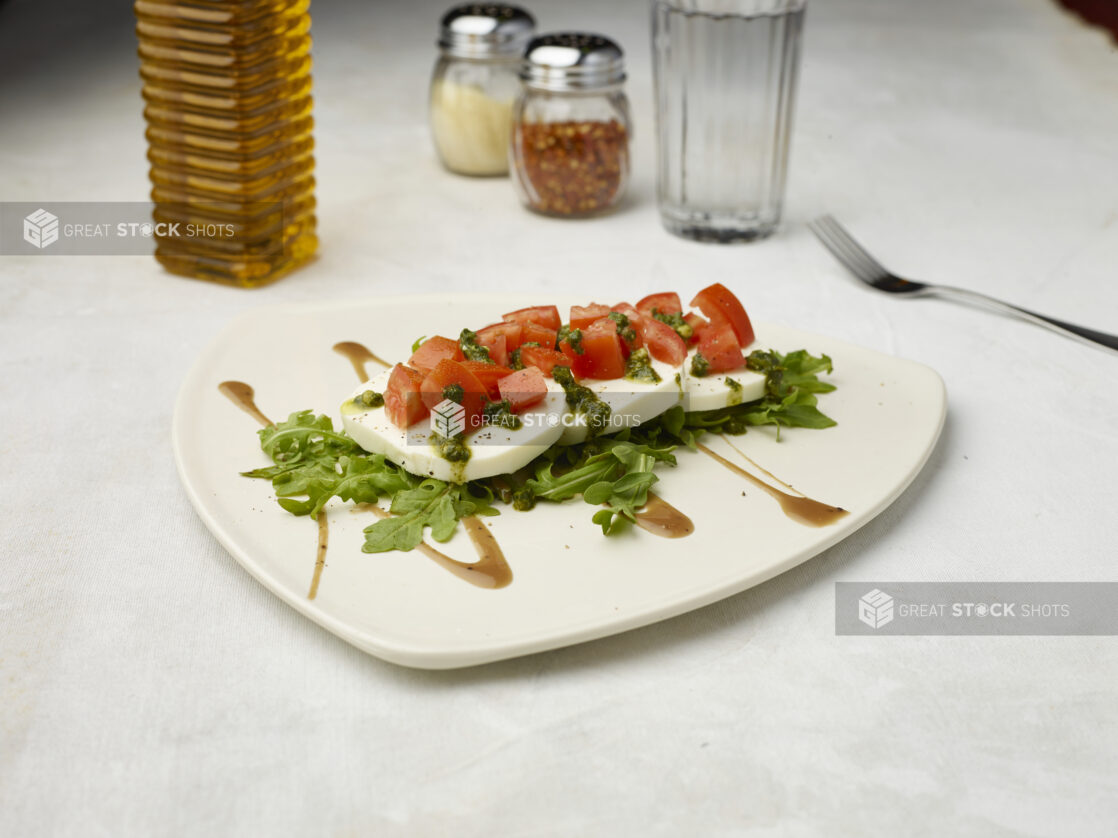 Caprese salad drizzled with pesto and sauce on the bottom on a white background