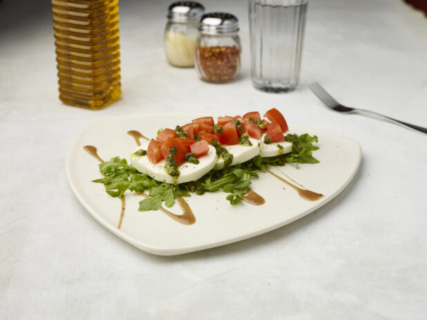 Caprese salad drizzled with pesto and sauce on the bottom on a white background