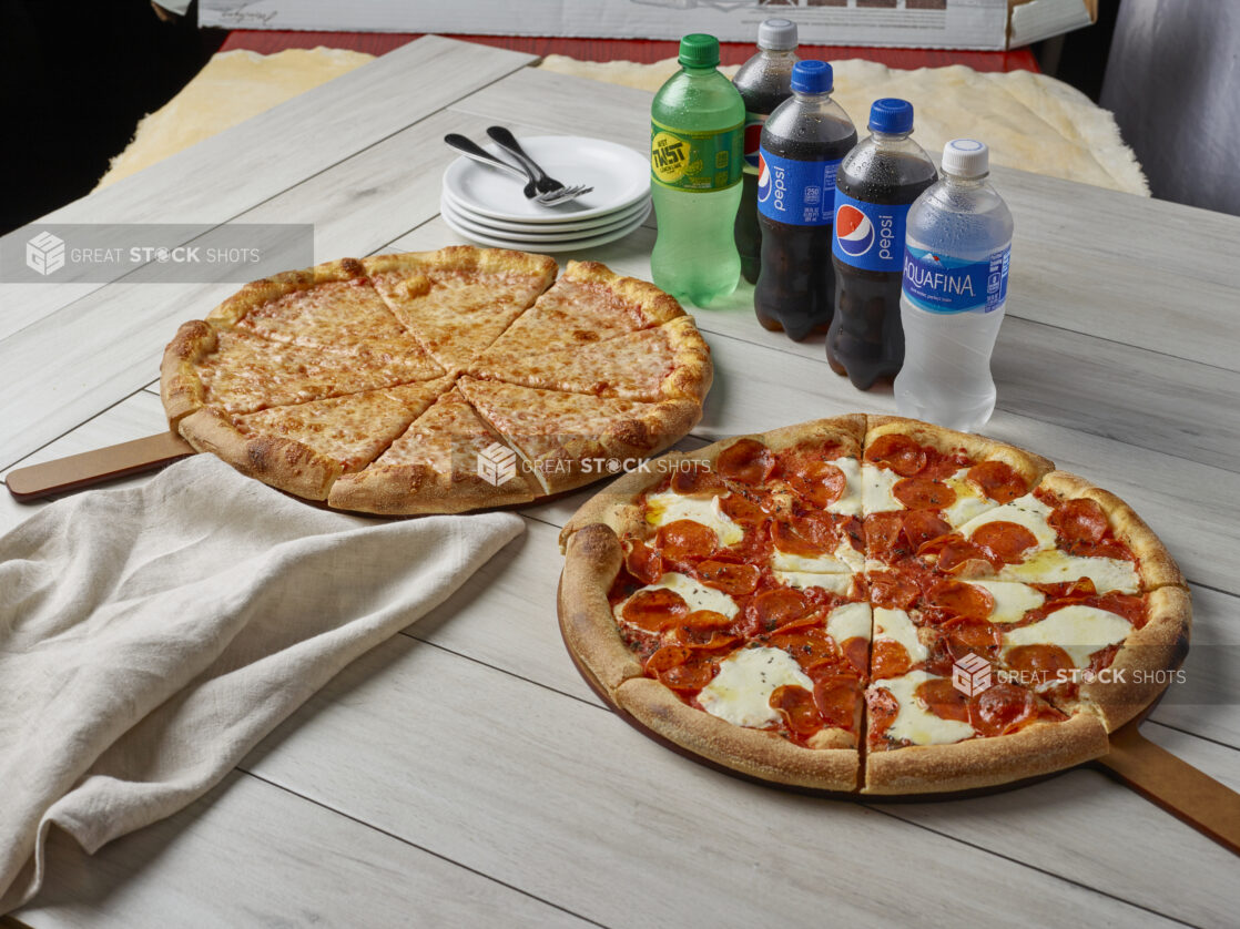 Two pizzas, one with cheese and the other with pepperoni and fresh mozzarella with drinks on a wooden background