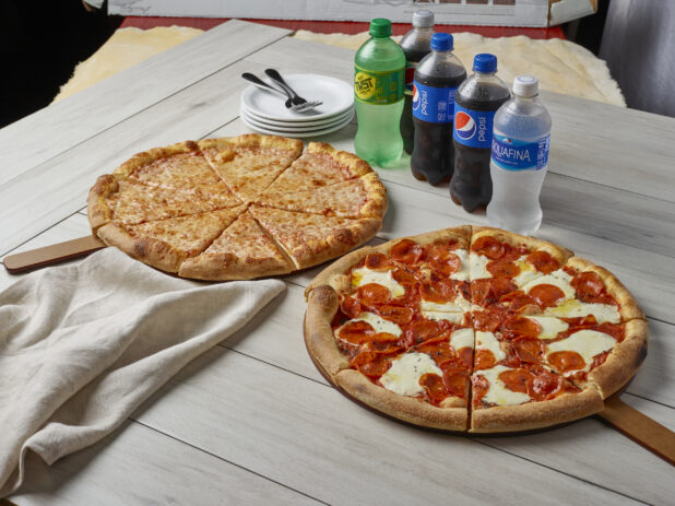 Two pizzas, one with cheese and the other with pepperoni and fresh mozzarella with drinks on a wooden background