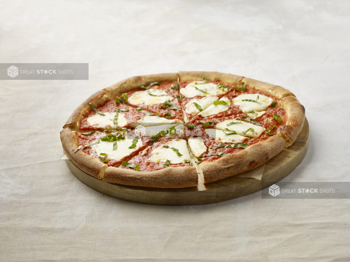 Sliced margherita pizza on a wooden board with parchment paper