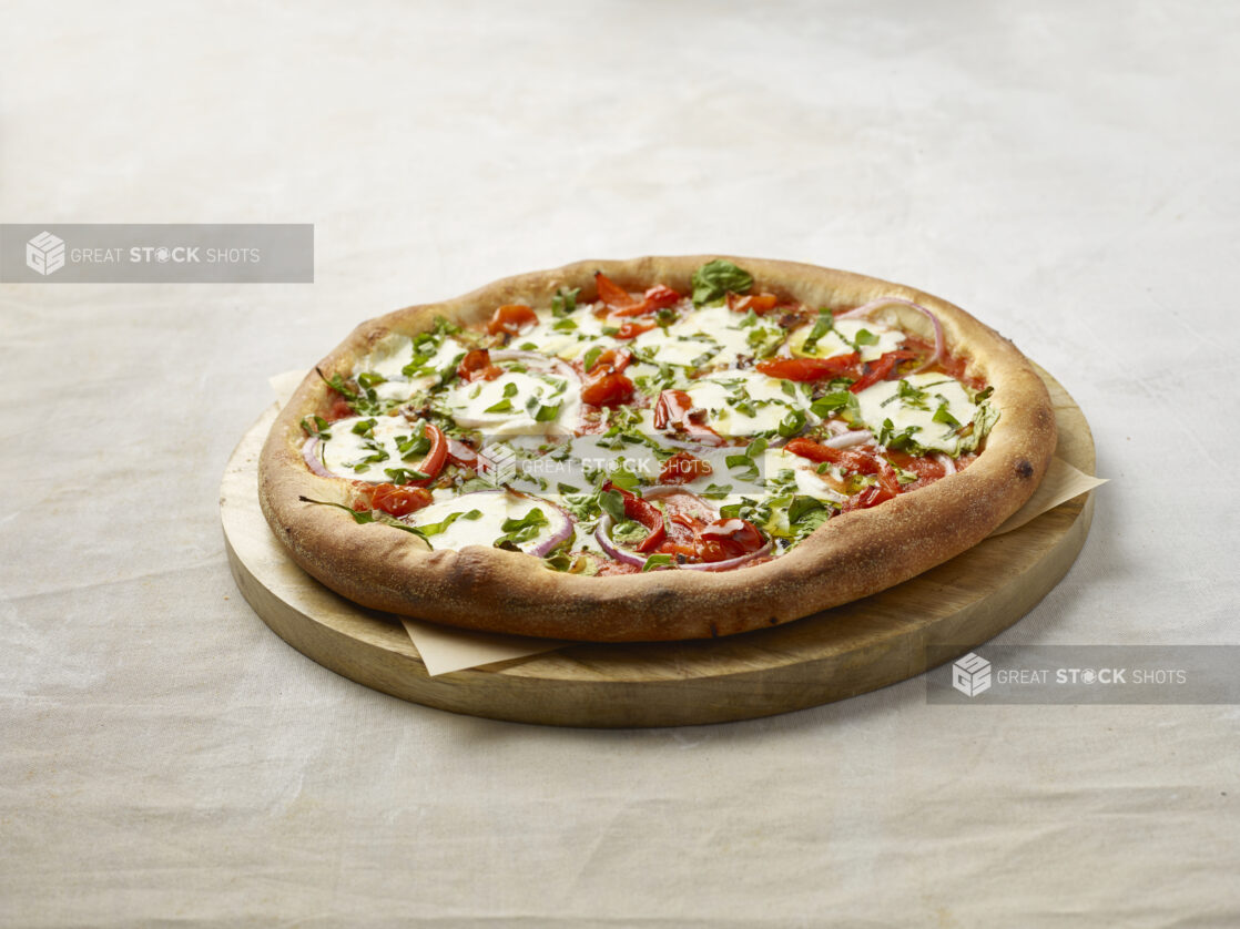 Whole pizza with red pepper, spinach and onion topped with fresh basil with a slice missing on a wooden board with parchment paper