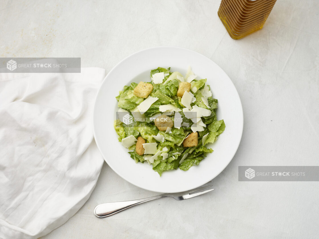 Overhead view of Caesar salad with white napkin on a white table cloth