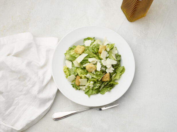 Overhead view of Caesar salad with white napkin on a white table cloth