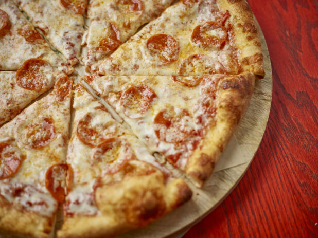 Pepperoni and cheese pizza close up on a wooden board with a red wood background