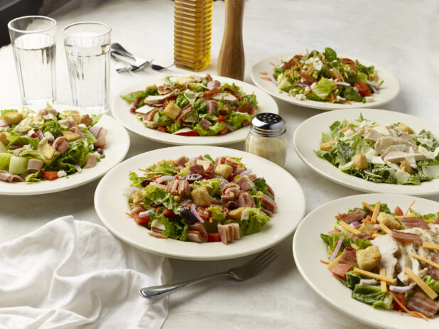 Multiple bowls of salad on a light table cloth with two glasses of water