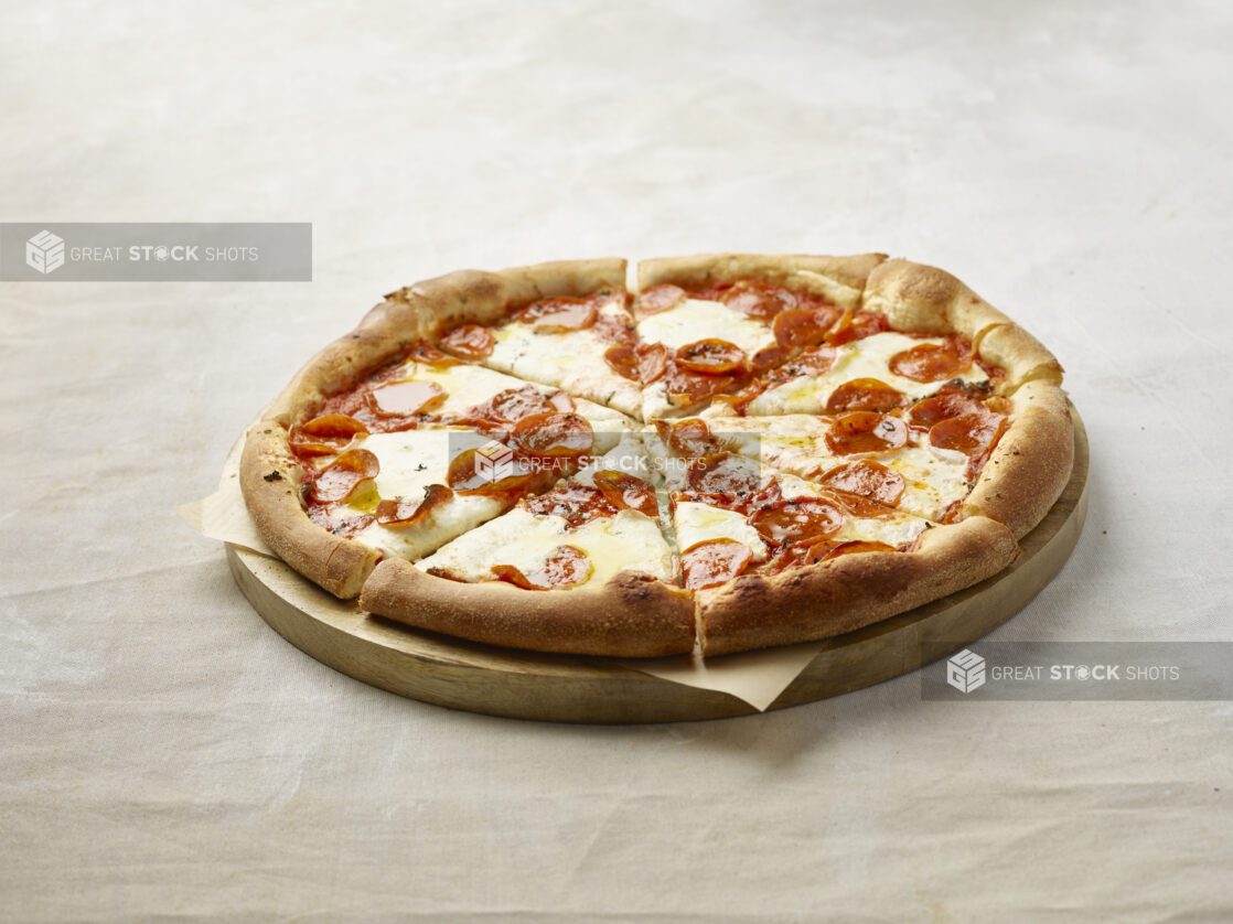 Sliced pepperoni pizza on a wooden board with parchment paper