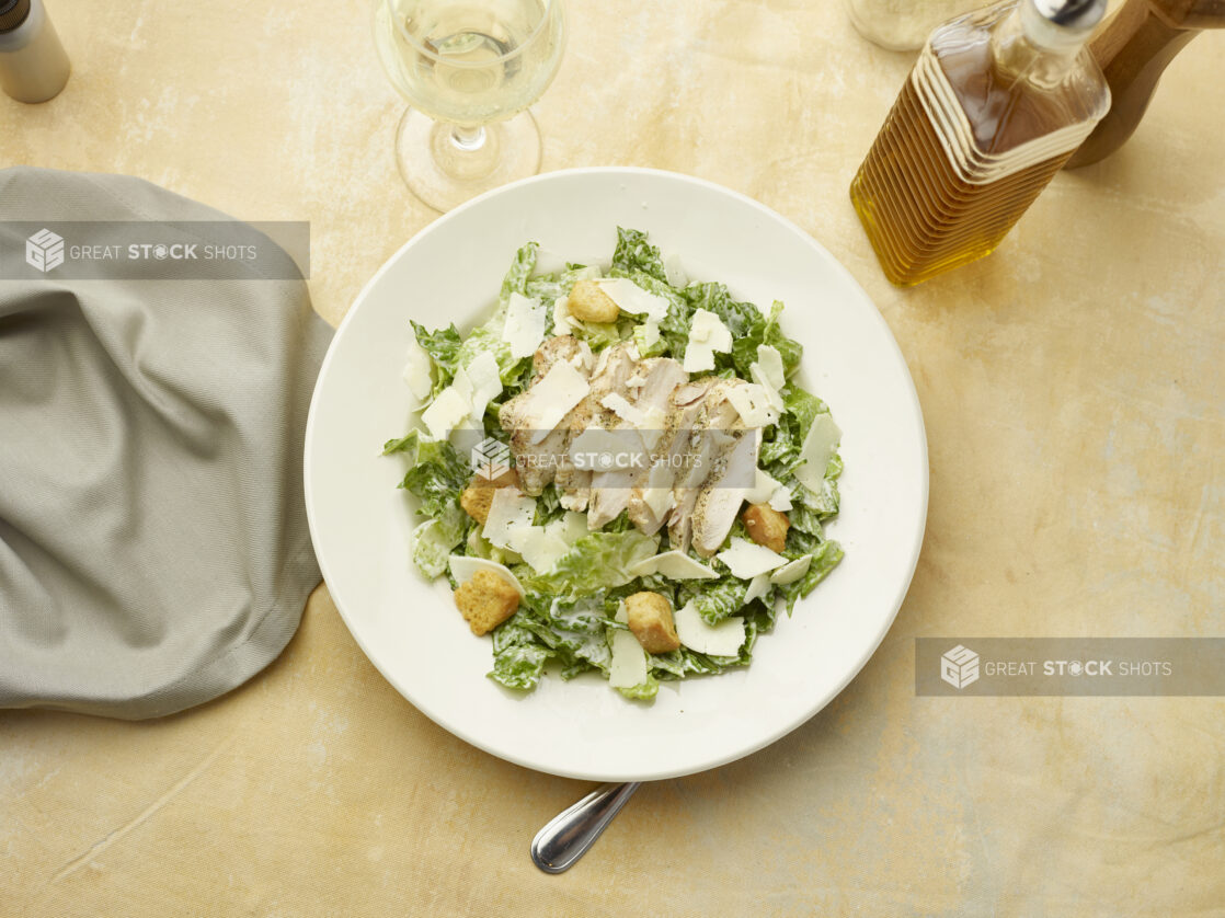 Overhead view of Caesar salad with a glass of white wine on a beige background