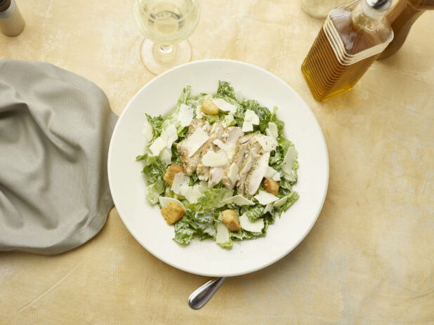 Overhead view of Caesar salad with a glass of white wine on a beige background