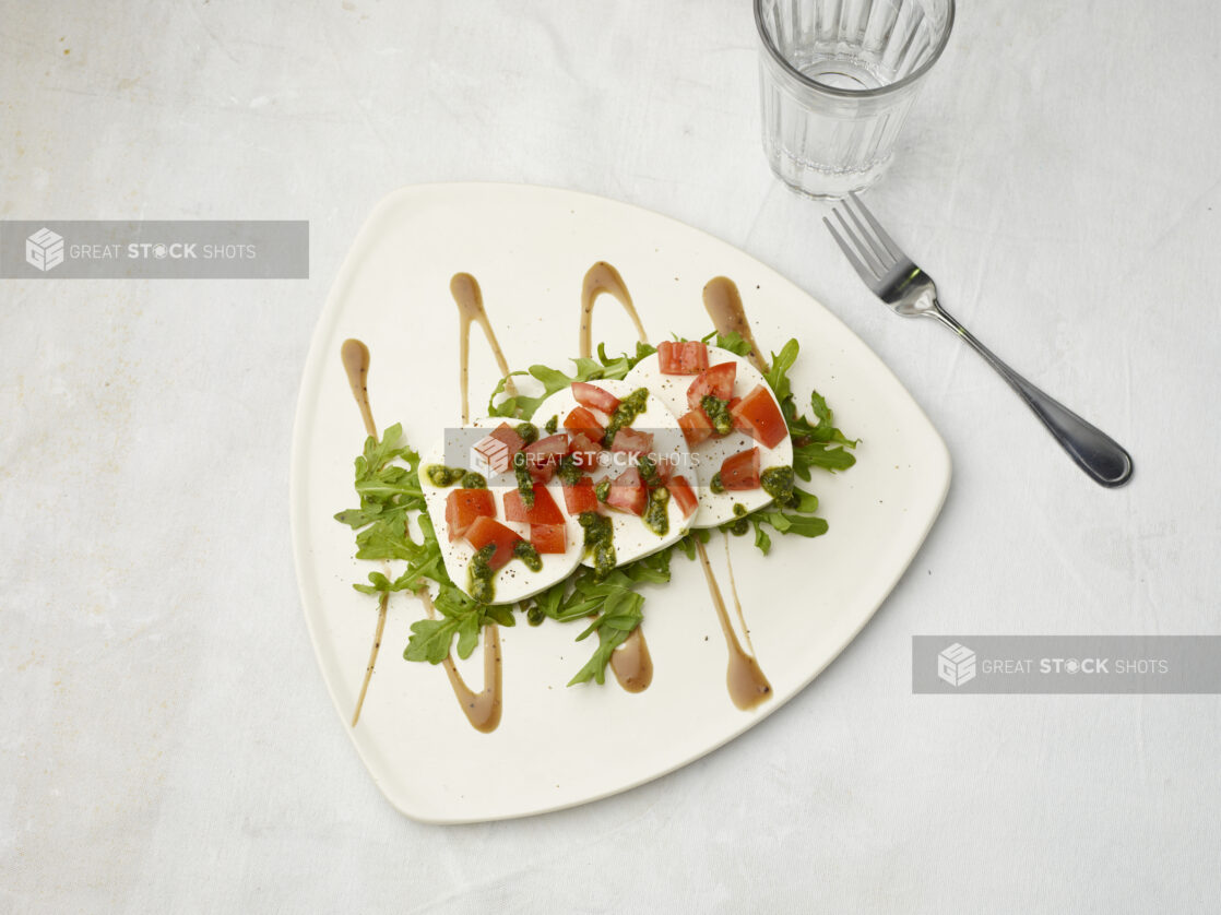 Overhead view of caprese salad drizzled with pesto and sauce on the bottom on a white background