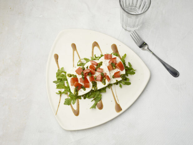 Overhead view of caprese salad drizzled with pesto and sauce on the bottom on a white background