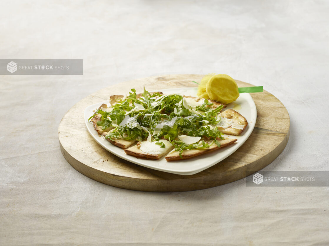 Sliced flatbread with melted cheese, topped with arugula and shaved parmesan on a wooden board