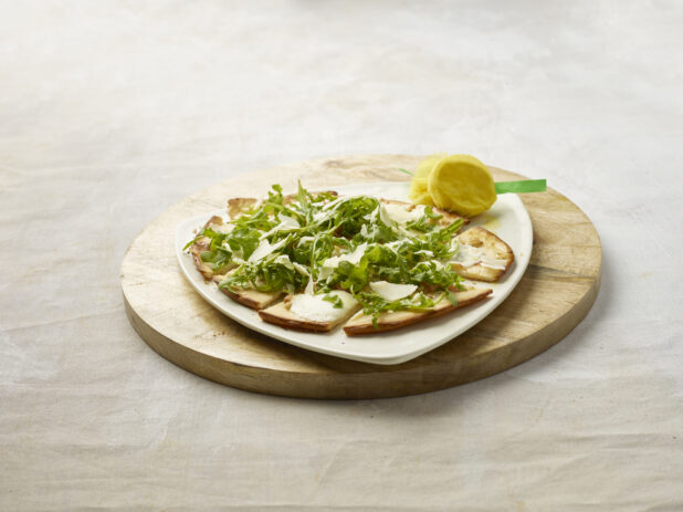 Sliced flatbread with melted cheese, topped with arugula and shaved parmesan on a wooden board