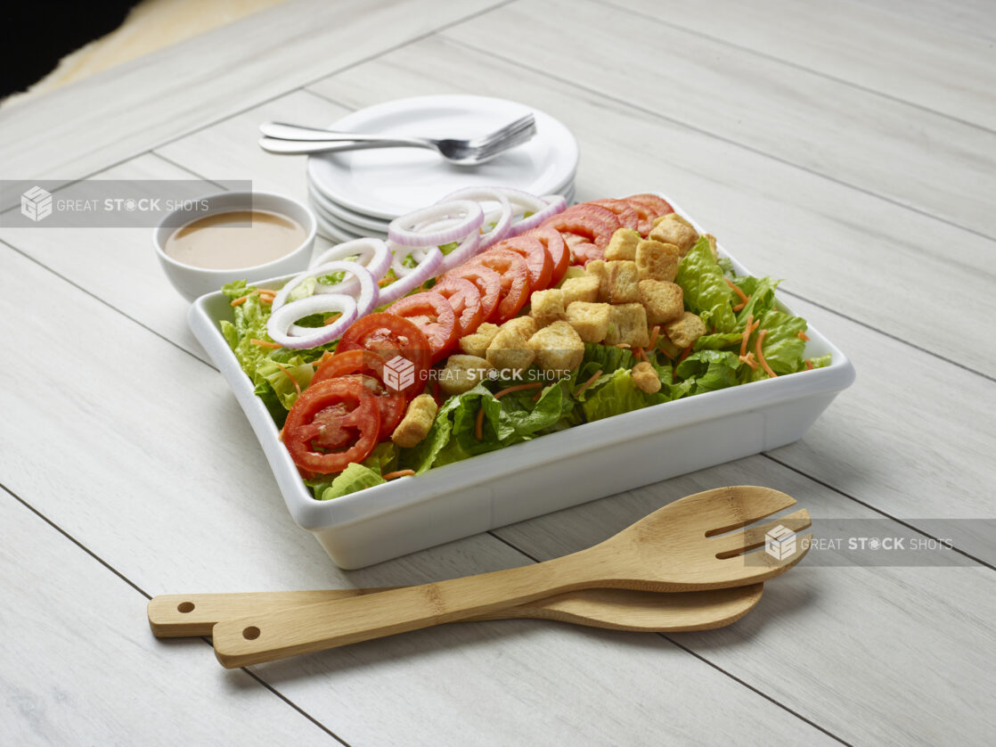 Large garden salad with dressing on the side and servewear in the background