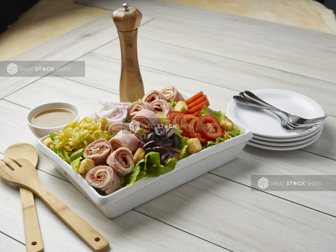 Large salad with rolled meats and a side dressing with servewear in the background