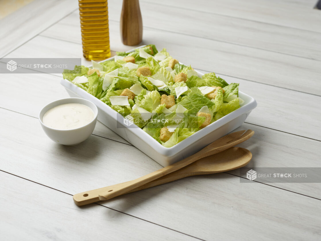 Large Caesar salad with dressing on the side and servewear in the background