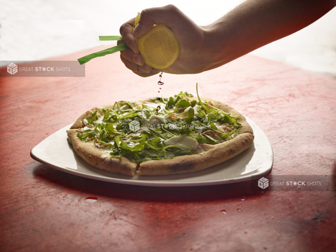 Hand squeezing fresh lemon in a cheese cloth on a sliced pizza topped with arugula