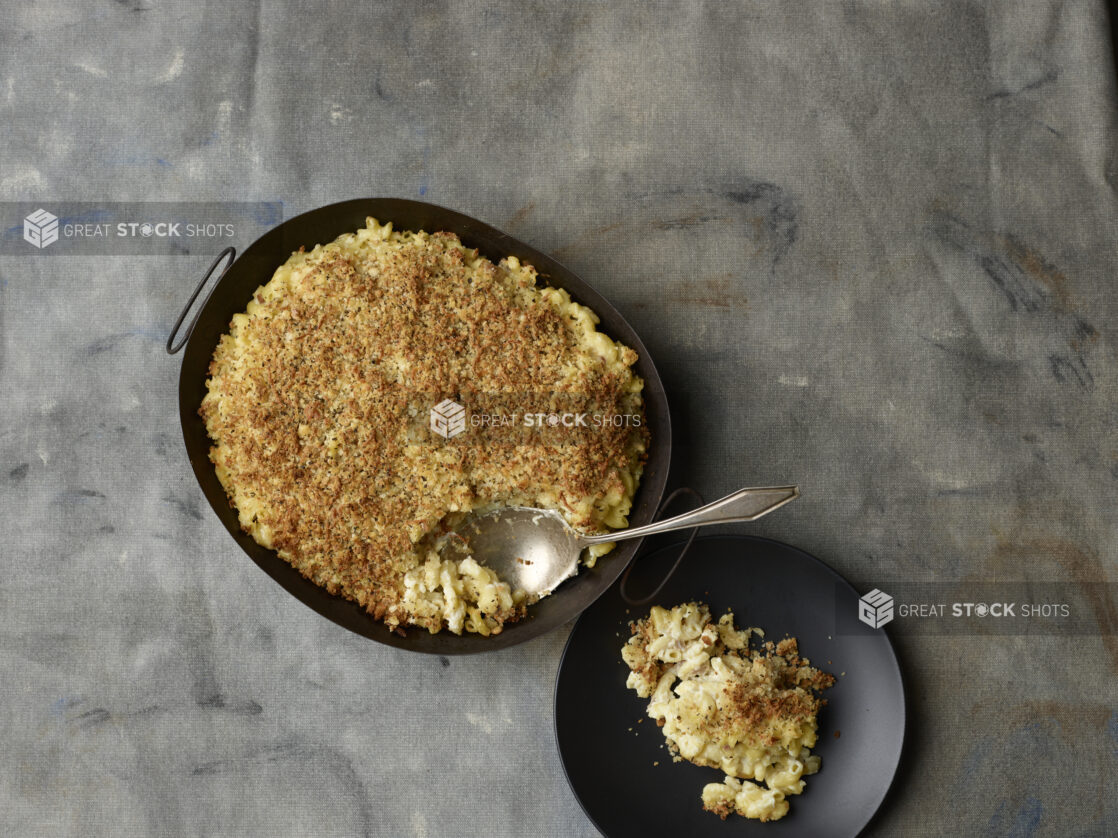 Large family sized portion of mac and cheese with a crunchy topping with a portion spooned on to a plate