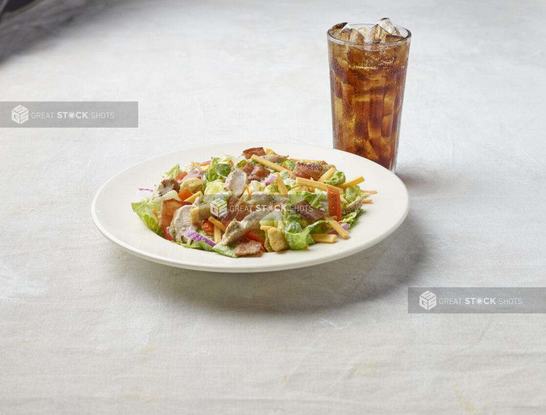 Bowl of chicken bacon garden salad on a light background with a glass of cola