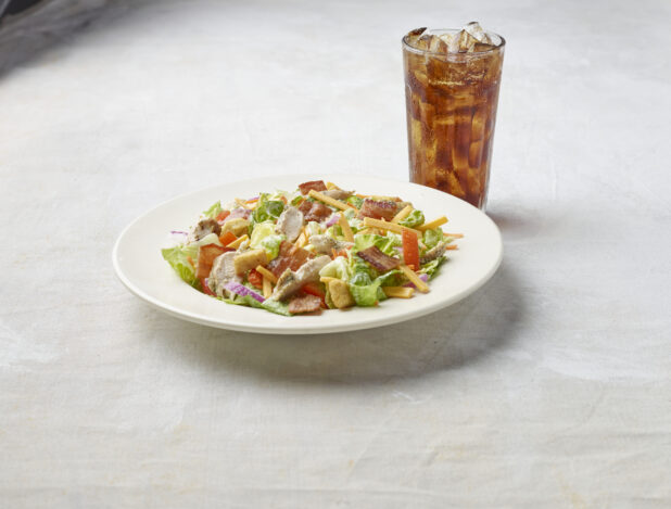 Bowl of chicken bacon garden salad on a light background with a glass of cola