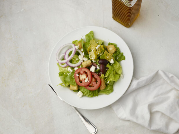 Overhead view of Greek salad with napkin on a white table cloth