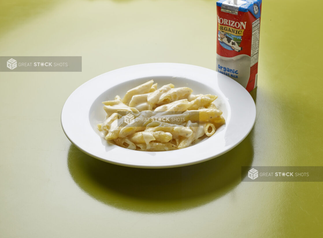 Kids meal of penne with Alfredo sauce with drink box of milk on a green background