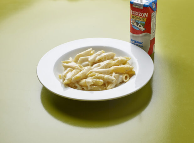 Kids meal of penne with Alfredo sauce with drink box of milk on a green background