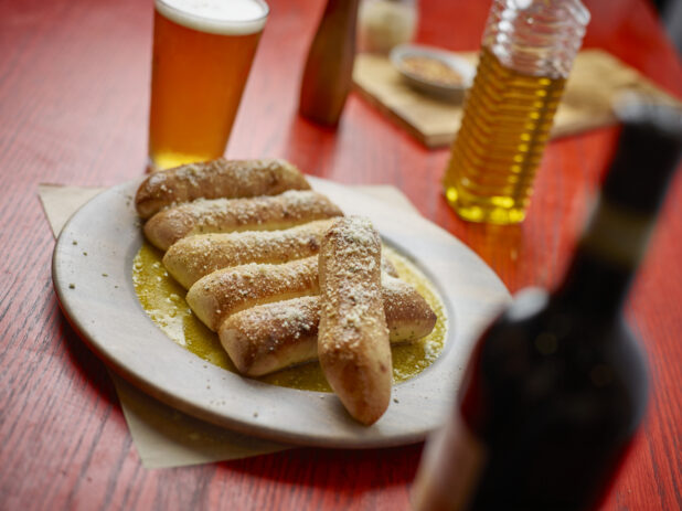 Order of garlic bread sticks on a white plate with a beer on a red wooden table