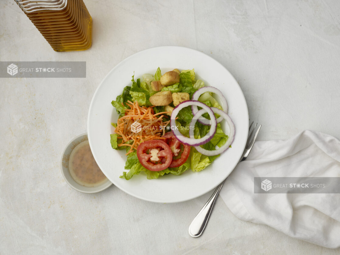 Overhead view of garden salad with dressing on the side on a white table cloth