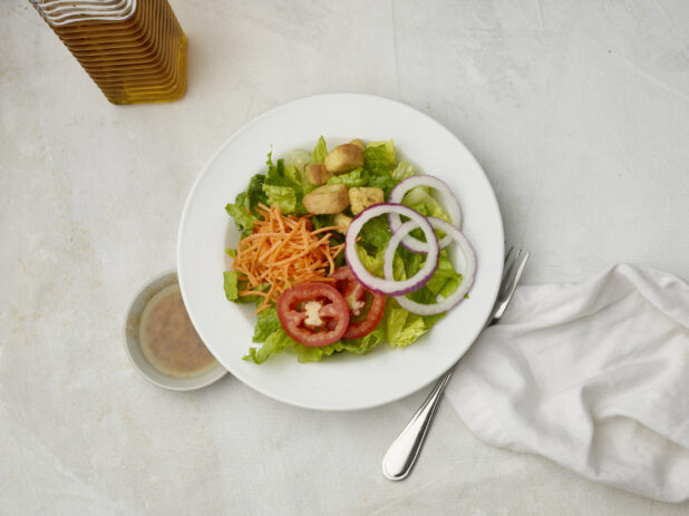 Overhead view of garden salad with dressing on the side on a white table cloth