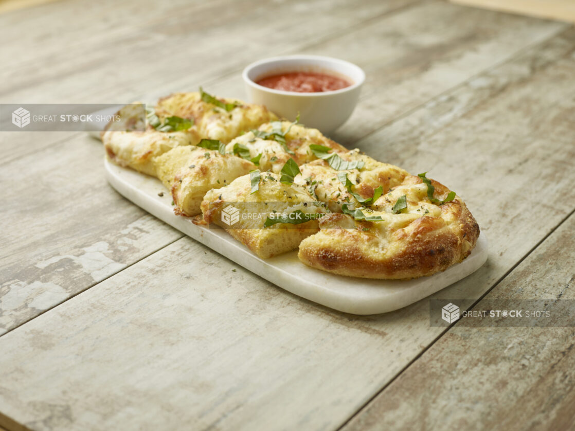 Cut garlic cheese bread topped with fresh basil on a marble board with a side of tomato sauce