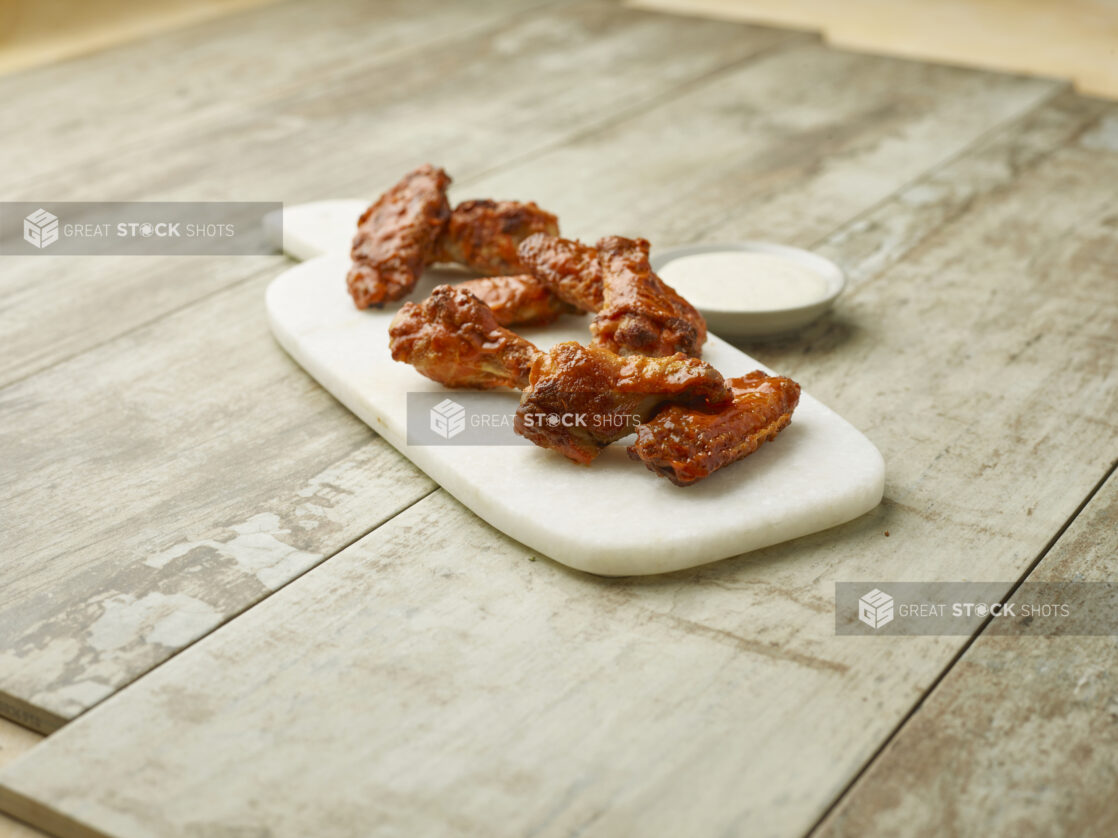 Sauced chicken wings on a marble board with a creamy dipping sauce on a wooden background