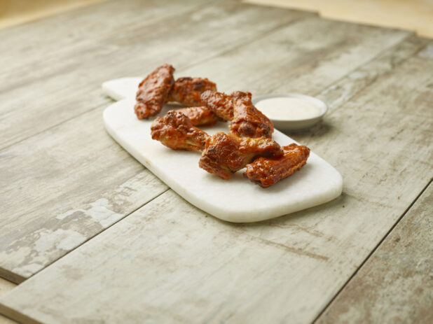 Sauced chicken wings on a marble board with a creamy dipping sauce on a wooden background
