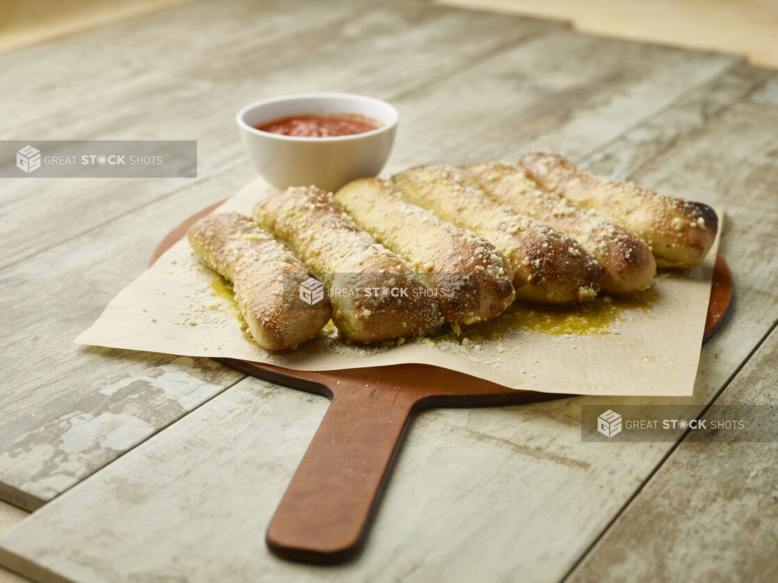 Order of garlic bread sticks on parchment paper on a wooden board with tomato dipping sauce