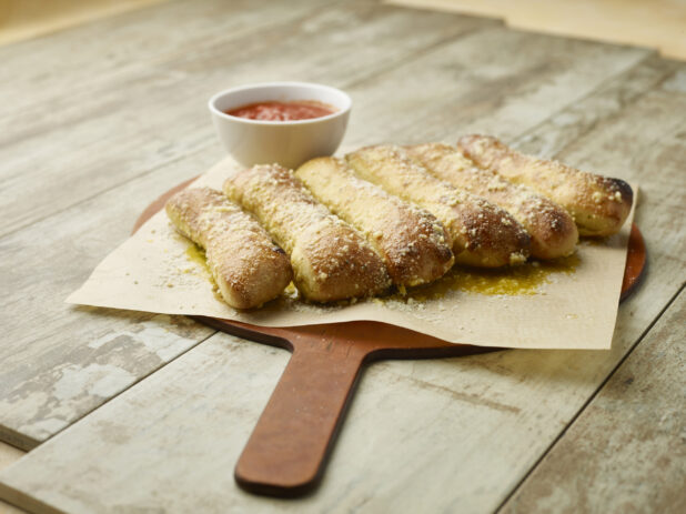 Order of garlic bread sticks on parchment paper on a wooden board with tomato dipping sauce