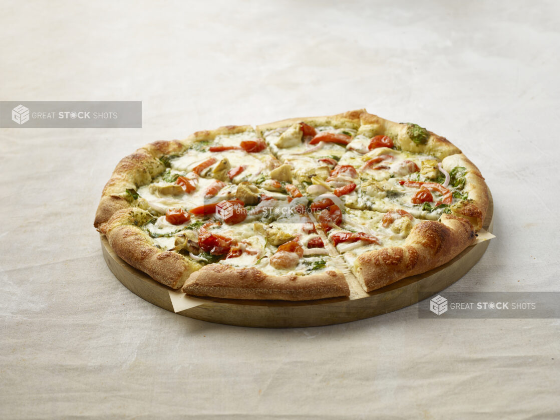 Sliced pizza with cherry tomatoes, red pepper, artichoke, spinach and onion with a pesto base on a wooden board with parchment paper