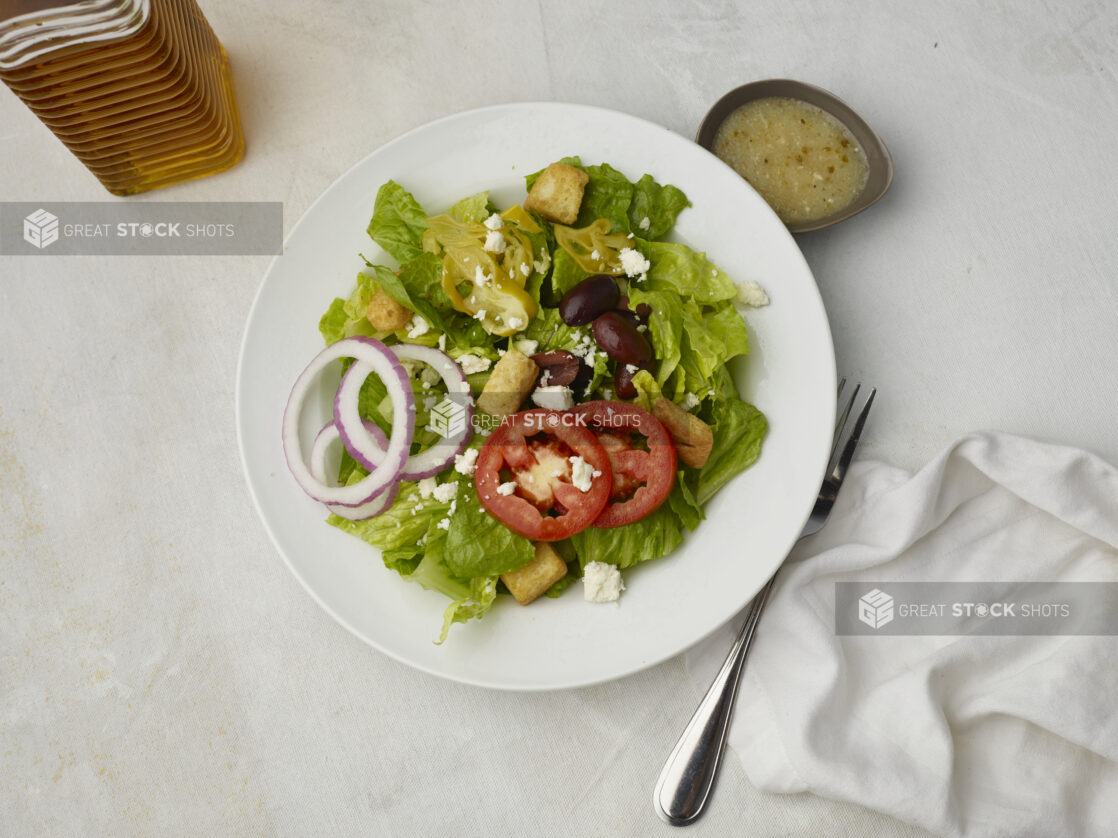 Overhead view of Greek salad with dressing on the side on a white table cloth