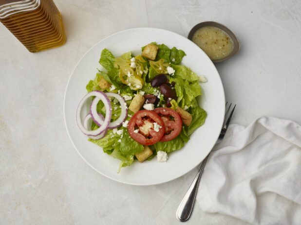 Overhead view of Greek salad with dressing on the side on a white table cloth