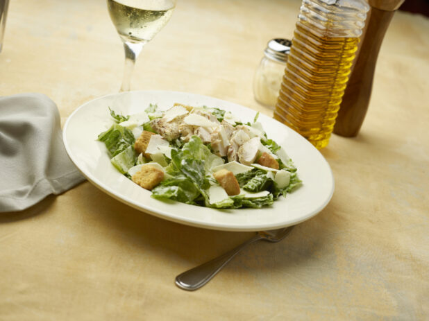 Caesar salad with a glass of white wine on a beige background