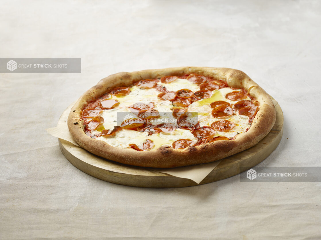 Whole pepperoni pizza on a wooden board with parchment paper