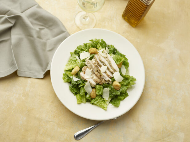 Overhead view of Caesar salad with a glass of white wine on a beige background