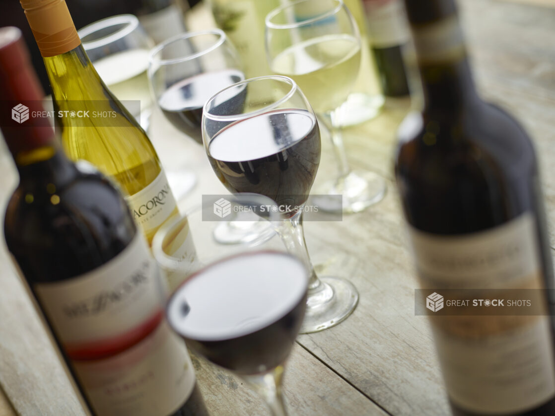 Multiple wine glasses of red and white with wine bottles on a wooden background