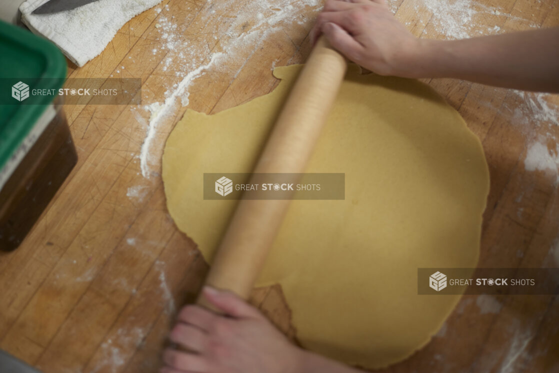 Baker rolling out dough on a floured wood board