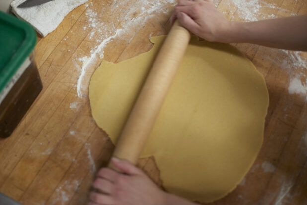 Baker rolling out dough on a floured wood board