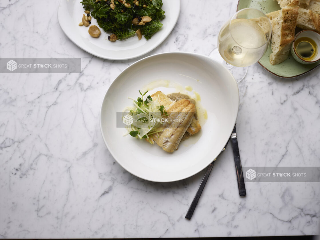 Two fillets of white fish, drizzled with butter and garnished with microgreens, white marble background