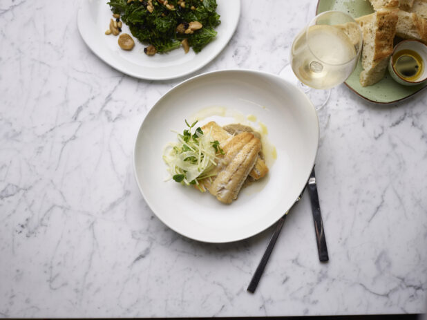 Two fillets of white fish, drizzled with butter and garnished with microgreens, white marble background