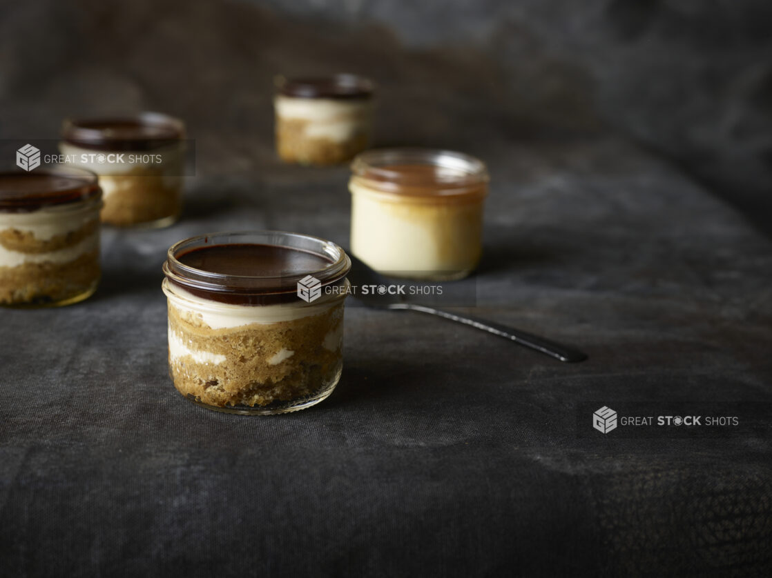 Small individual serving mason jars of tiramisu on a black cloth background, close-up