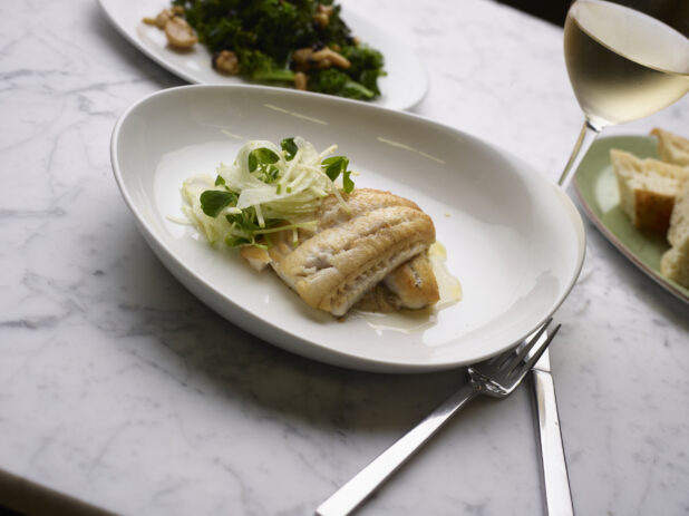 Pan-fried white fish with mixed microgreens on a white plate, white marble background