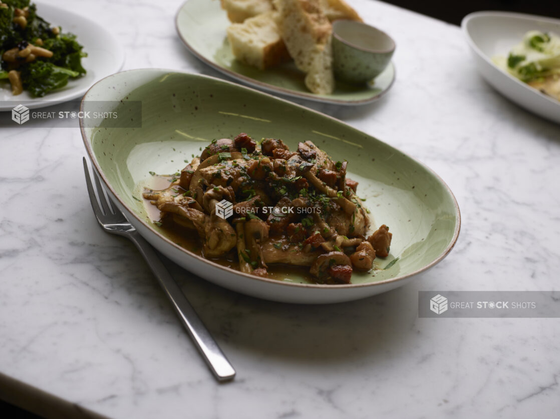 Chicken Marsala with Caramelized Button Mushrooms in a Green Ceramic Dish on a Marble Table