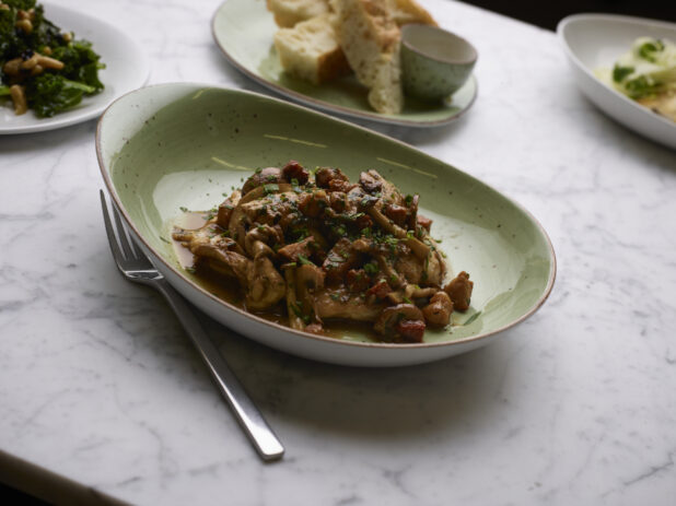 Chicken Marsala with Caramelized Button Mushrooms in a Green Ceramic Dish on a Marble Table